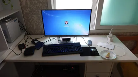 Desk by a window with a monitor, keyboard, mouse and a small PC