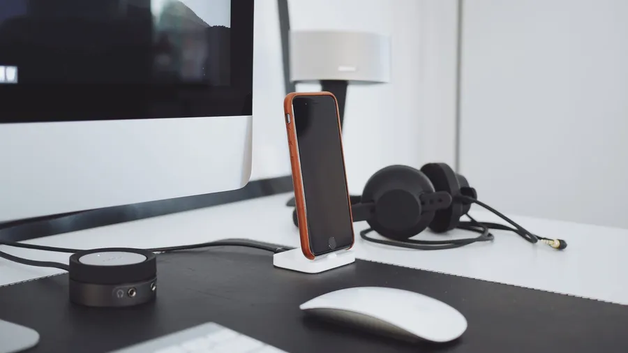 Desk with a monitor, a phone on a dock, headphones and a mouse