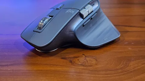 Grey ergonomic mouse with thumb buttons on a wooden desk