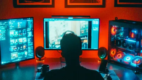 A gamer viewed from behind, sitting at a multi-monitor desktop setup with an open PC case