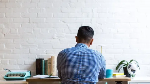 Person sitting at a desk facing a white brick wall