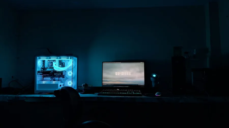 Gaming PC with blue internal lighting next to a monitor in a dark room