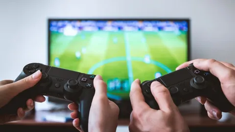 Two players holding controllers in front of a TV showing a football game