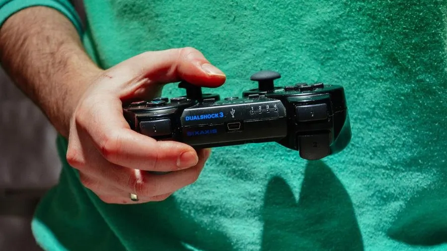 Hand holding a PlayStation controller against a green background