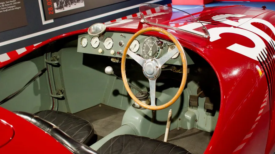 Wooden-rimmed steering wheel and dashboard gauges inside a red vintage race car