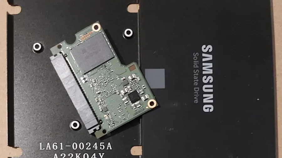 Samsung 2.5-inch solid state drive opened up, with its small green circuit board lying on the black metal case beside the lid