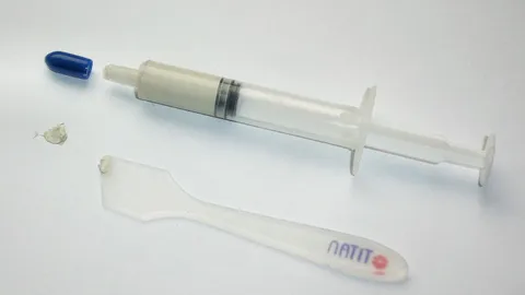 Syringe of grey thermal paste next to a plastic spreading spatula