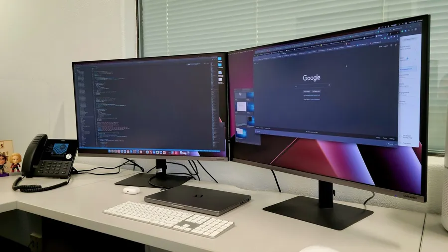 Two monitors side by side on an office desk with a keyboard and phone